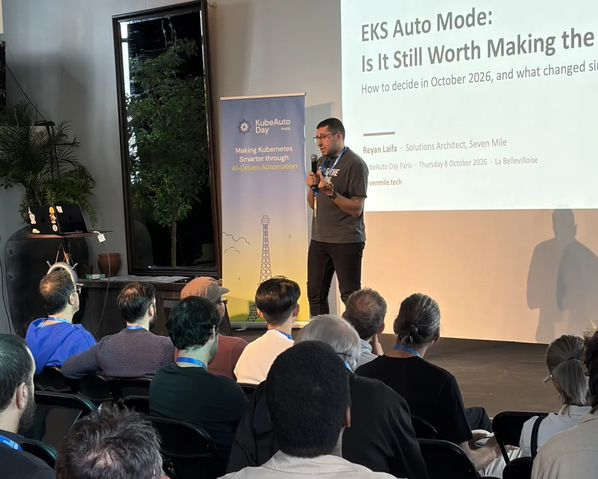 Reyan Laifa au micro sur la scène de KubeAuto Day Paris, devant la slide de titre du talk sur EKS Auto Mode